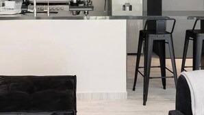 A modern kitchen with a central island, bar stools, and a dining area with a white couch. - Suave Polanco Exclusive - Modern 2-bedroom Apartment in Polanco (Mexico City)