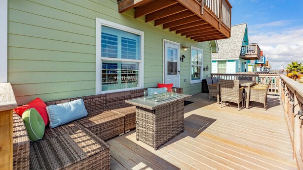 Una terraza cubierta al aire libre con muebles de mimbre, una mesa con superficie de vidrio y barandilla de madera.