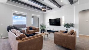 A spacious living room with leather sofas, a coffee table, and a flat-screen TV mounted on the wall. - 4-bedroom + Hot tub + Firepit + Sandia views (Rio Rancho)
