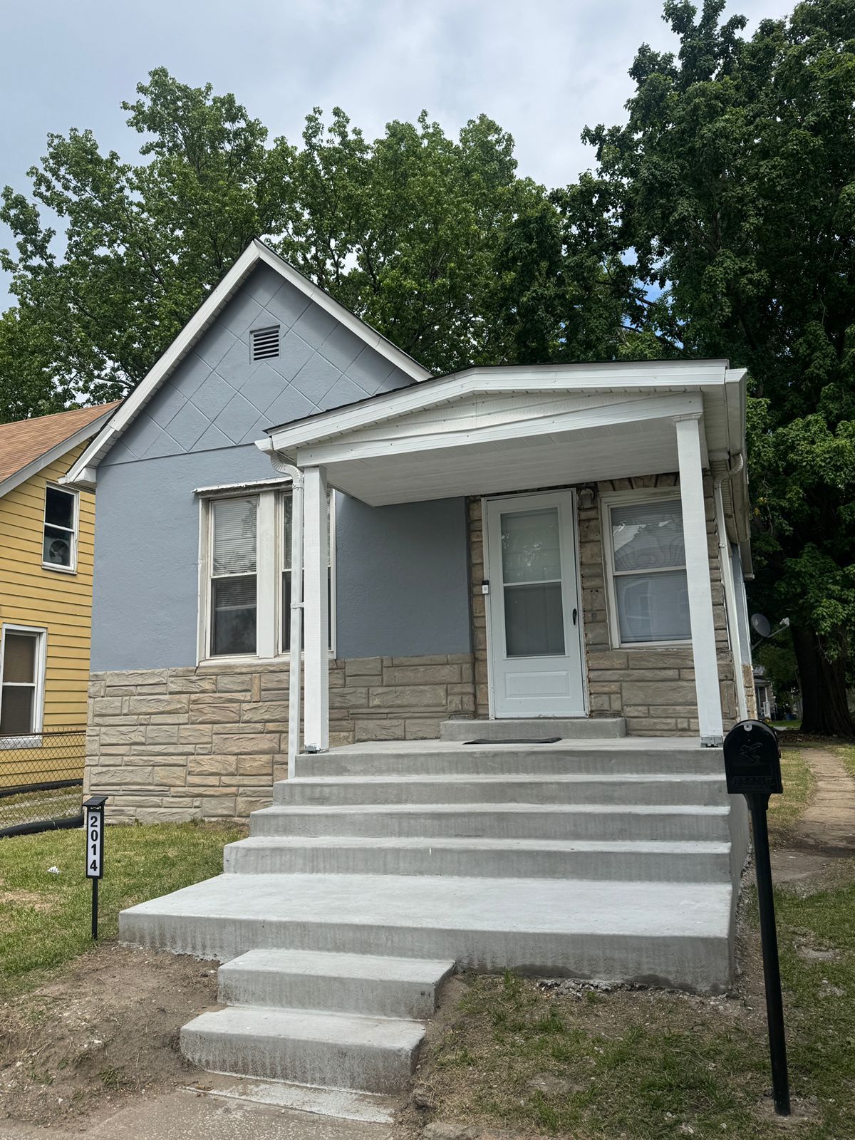 A two-story house with a front porch, a stone foundation, and a grey roof.