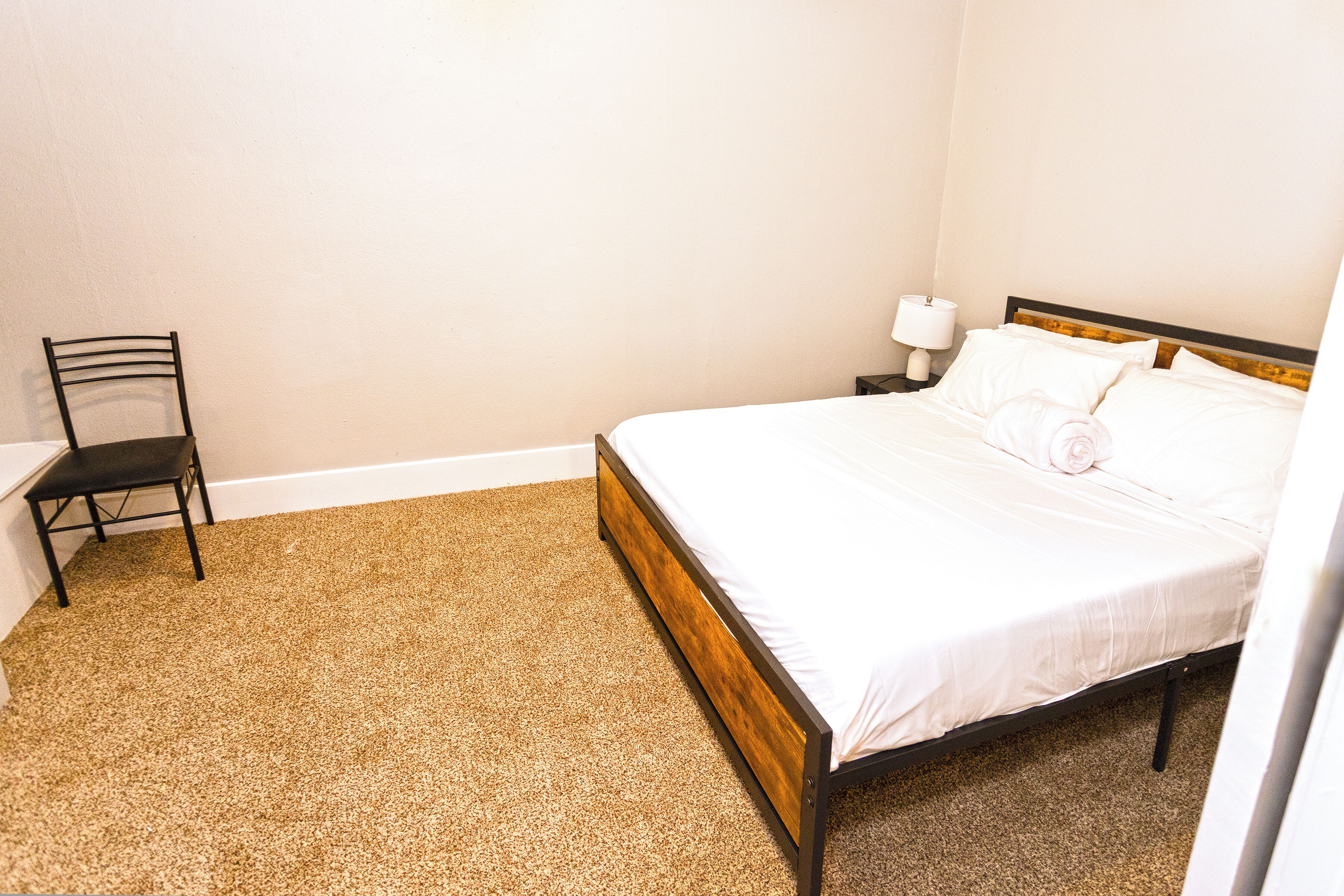 A bedroom with a bed, a chair, and a nightstand with a lamp.