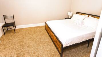 A bedroom with a bed, a chair, and a nightstand with a lamp.
