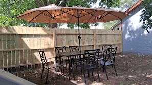Un patio al aire libre con mesa y sillas, un parasol colgante y una valla de madera.