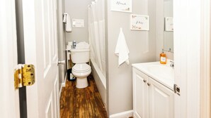 A narrow bathroom with a toilet, a sink, and a shower curtain. There are towels hanging on the wall and a bottle of hand soap on the sink. - Comfy, Quiet, Clean & Affordable! Great Location! Best bang for your buck! (Granite City)