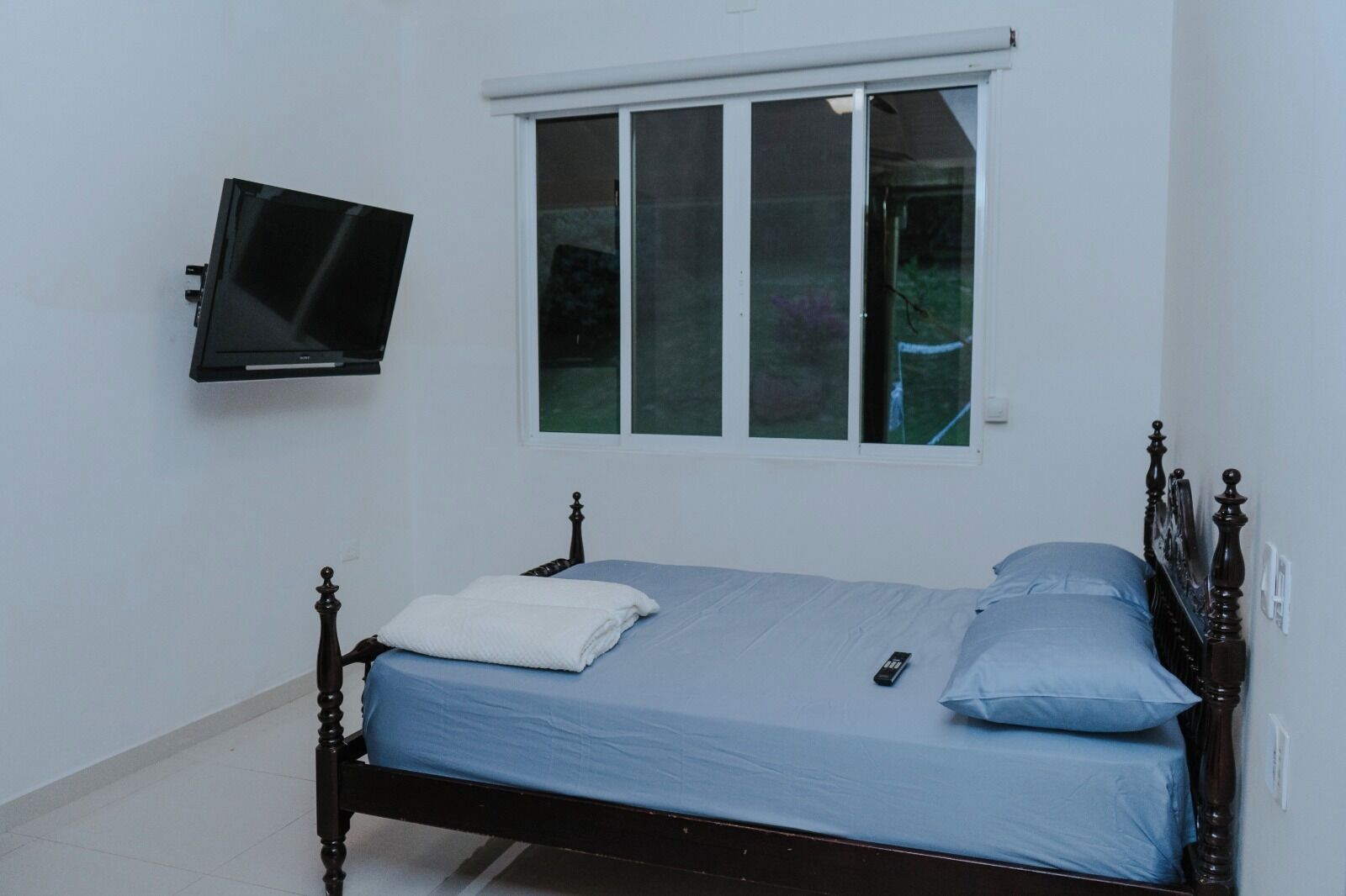 A bedroom with a bed, a television mounted on the wall, and a window.