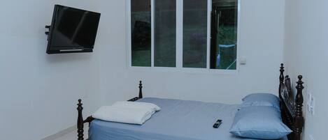 A bedroom with a bed, a television mounted on the wall, and a window.