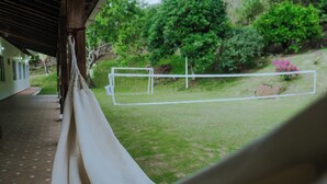 Een hangmat onder een overdekt terras met uitzicht op een gazon en bomen.