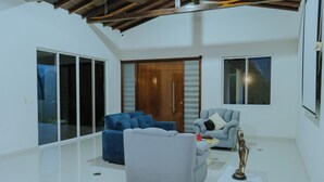 A spacious living room with a high ceiling, a sliding glass door leading to a balcony, and a large wooden door. - Villa Nogalito Piscinas, Cancha de Fútbol y Vistas a los Andes (San Gil)
