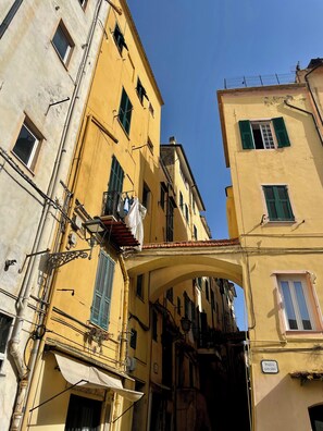 Una calle estrecha con edificios amarillos, un letrero que dice "Piazza San Siro" y ropa tendida en un balcón.
