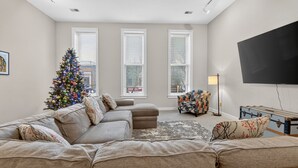 Una sala de estar con un sofá color crema, un árbol de Navidad, un televisor de pantalla plana y una lámpara.