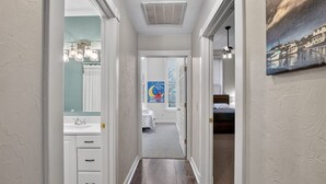 Un pasillo estrecho que conduce a un dormitorio con una cama, un baño con lavamanos y un pasillo con ventilador de techo.