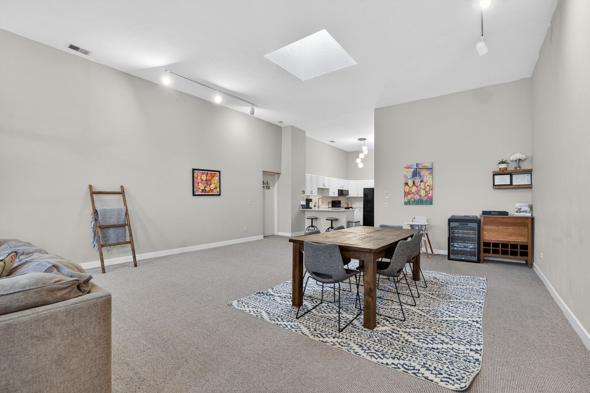 Una habitación amplia con una mesa de comedor, sillas, un sofá, una escalera y una cocina al fondo.