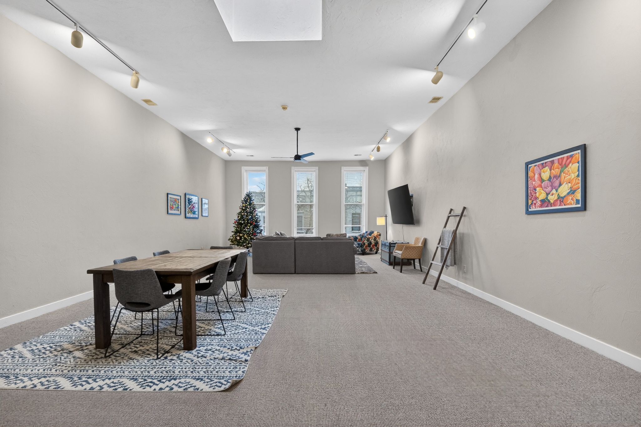 A spacious room with a dining area, a sofa, a Christmas tree, and a painting on the wall.