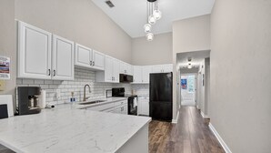 Una cocina moderna con armarios blancos, una isla grande de mármol y un refrigerador negro.