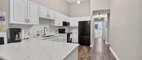 Una cocina moderna con armarios blancos, una isla grande de mármol y un refrigerador negro.