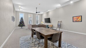 Un amplio salón con una mesa de comedor de madera, un árbol de Navidad, un sofá y un televisor montado en la pared.