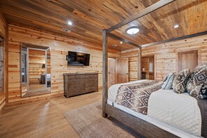 Une chambre dans un chalet en bois, avec un lit à baldaquin, une commode, un téléviseur fixé au mur et un miroir.
