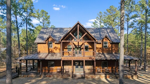 Une grande cabane en bois dotée d’un porche central, de nombreuses fenêtres et de fondations en pierre.