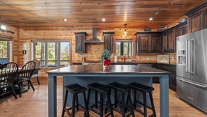 A spacious kitchen with a large island, wooden cabinetry, and a stainless steel refrigerator. - Spacious 5-bedroom cabin Centrally located in Hochatown with Backup Generator (Broken Bow)