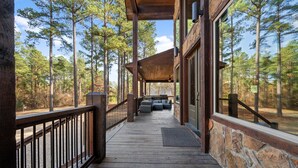 A wooden deck with stone walls, outdoor seating, and a view of a forest. - Spacious 5-bedroom cabin Centrally located in Hochatown with Backup Generator (Broken Bow)
