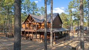Une cabane en rondins dotée d’un porche et de nombreuses fenêtres, entourée de grands arbres.