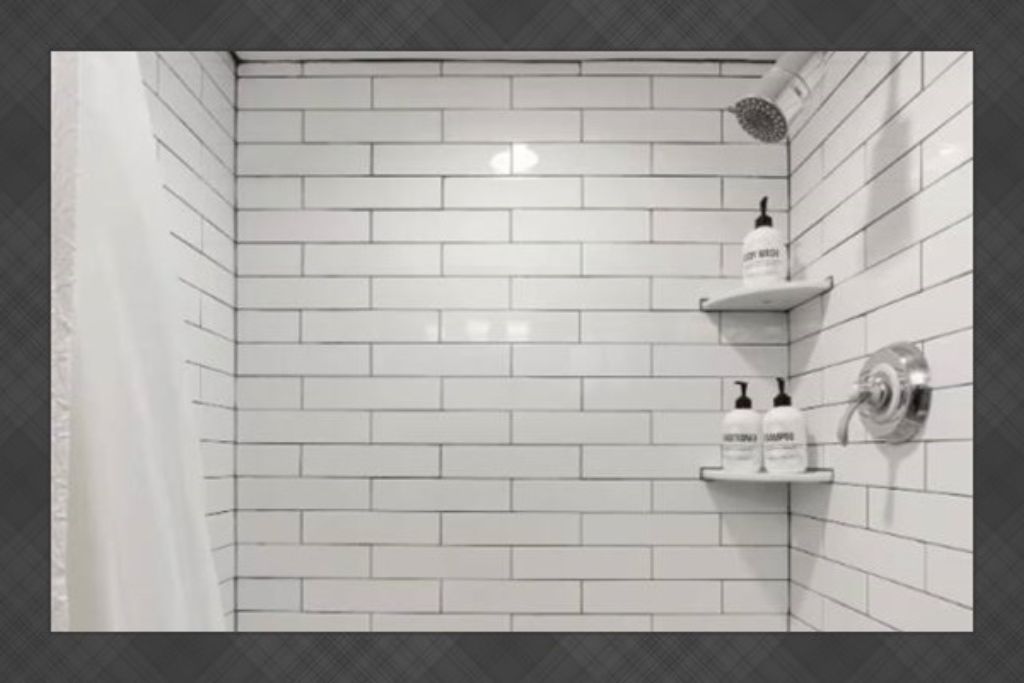 Un baño con azulejos blancos tipo metro, un cabezal de ducha y dos repisas con botellas.