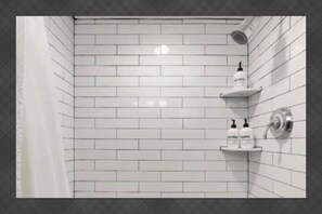 A bathroom with white subway tiles, a showerhead, and two shelves with bottles. - Pool | Game Yard · Old Town Views (Scottsdale)