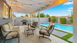 Um pátio externo com piscina, área de estar e luzes pendentes.