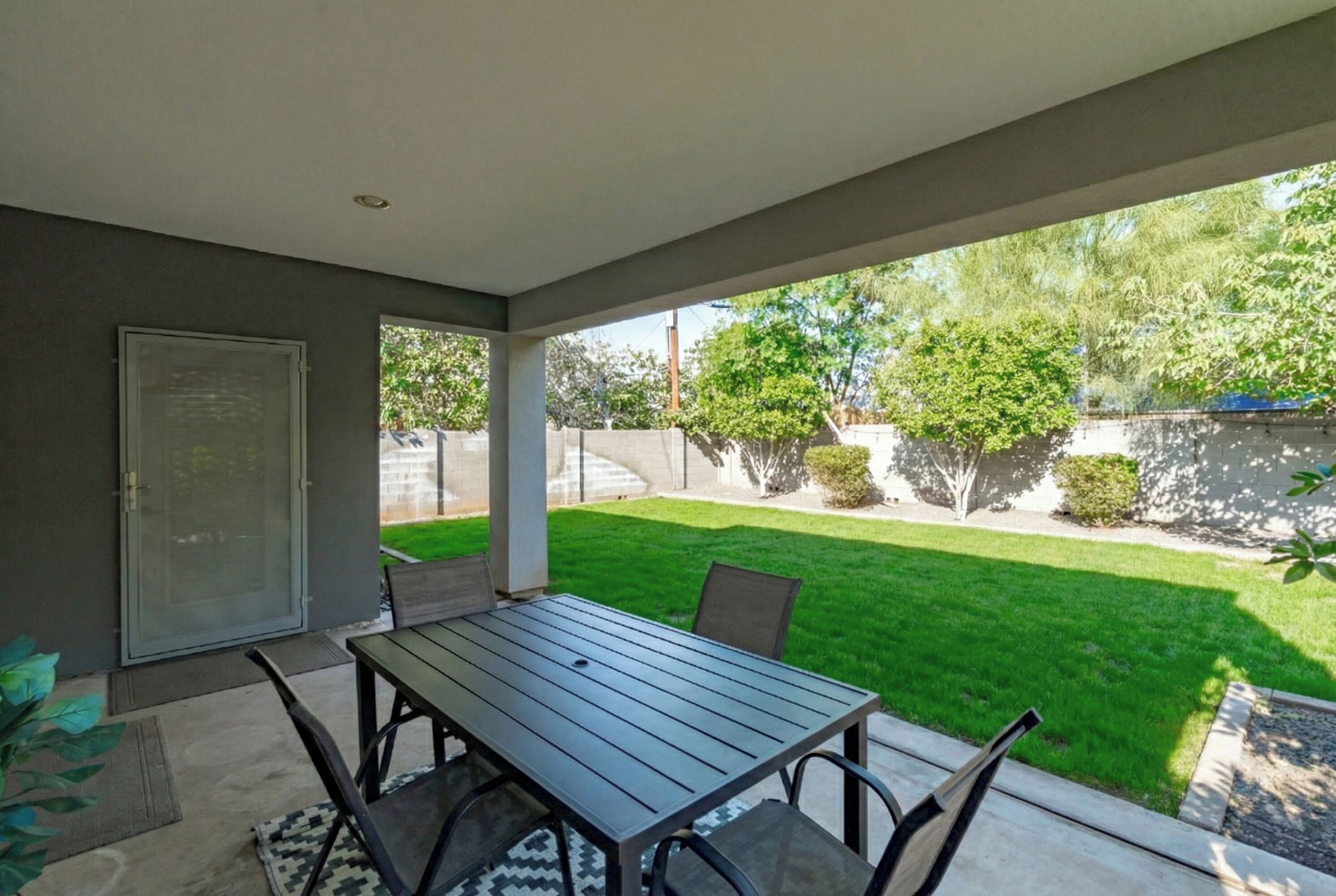 A covered patio with a table and chairs, a sliding glass door, and a view of a well-maintained lawn and trees.