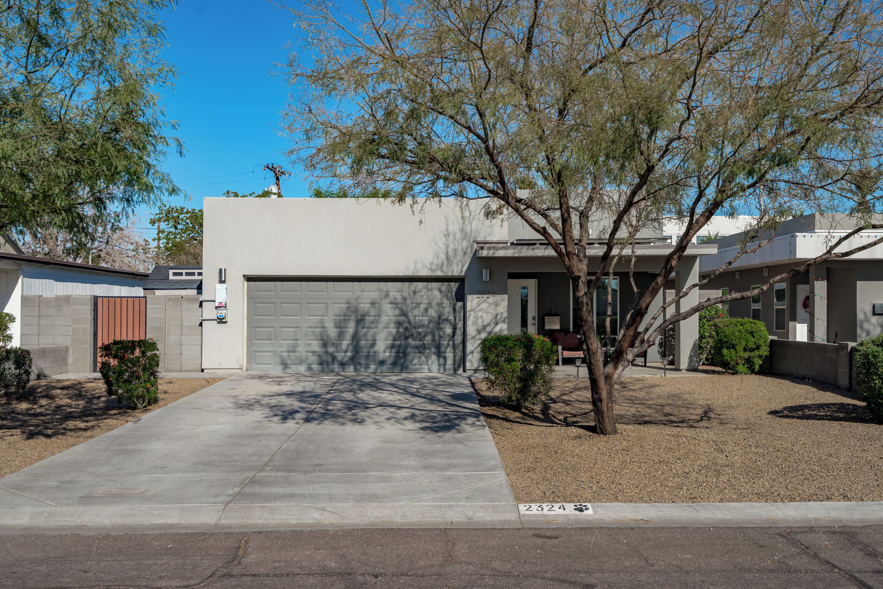 A residential house with a garage, a driveway, and a small tree in the front yard.