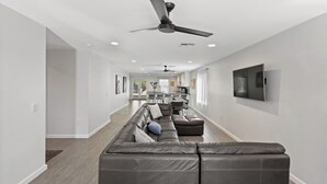 A modern living room with a sectional sofa, a ceiling fan, recessed lighting, and a TV mounted on the wall. - Bright Modern Home in Central Phx w/ Private Yard 8min to Airport & Downtown (Phoenix)