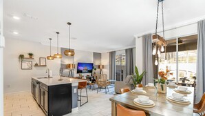 Cocina moderna con una isla central, comedor con mesa de madera dispuesta para cuatro personas y un televisor al fondo.
