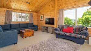 L’intérieur d’un chalet en bois chaleureux et accueillant, avec un canapé bleu, un canapé à carreaux, une table basse en bois et un téléviseur posé sur un meuble en bois.