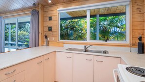 Une cuisine moderne avec des murs en bois, une grande fenêtre donnant sur un paysage verdoyant, un évier en acier inoxydable et une cuisinière blanche.