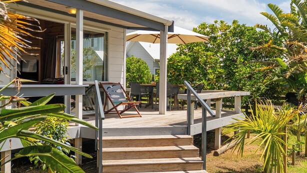 Une terrasse en bois avec des meubles d’extérieur, un espace salon couvert et un escalier menant à une maison.
