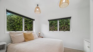 A bedroom with a bed, two windows, a bedside table, and a nightstand. - Rotoiti Escape - Lake Rotoiti Holiday Home (RD 4)