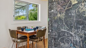 A dining area with a table set for two, a chalkboard wall with writings, and a window overlooking greenery. - Rotoiti Escape - Lake Rotoiti Holiday Home (RD 4)