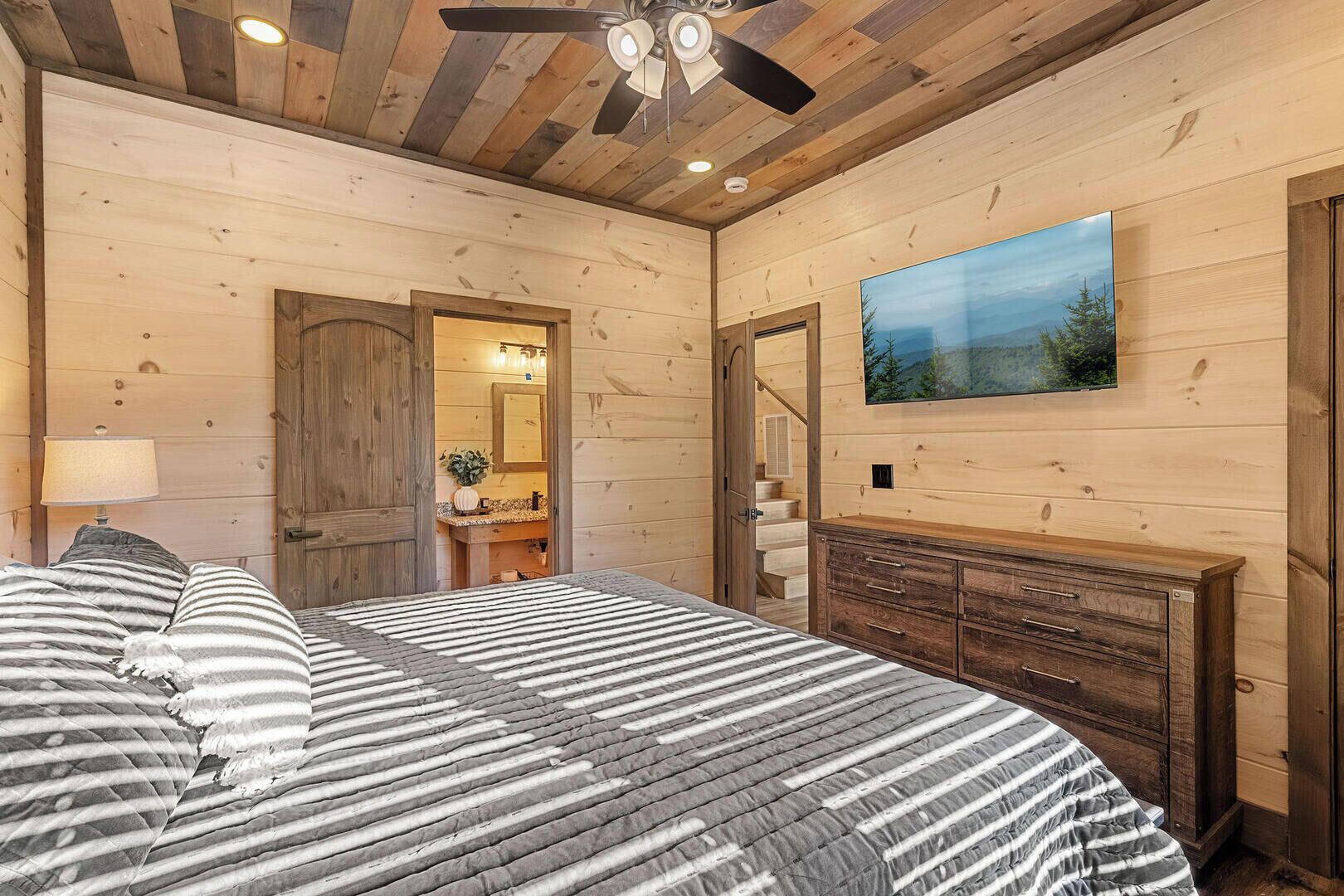 A bedroom with a bed, a dresser, a TV, and a staircase leading to a bathroom.