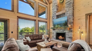 A spacious living area with a stone fireplace, leather sofas, and large windows. - Peaceful Paradise (Sevierville)
