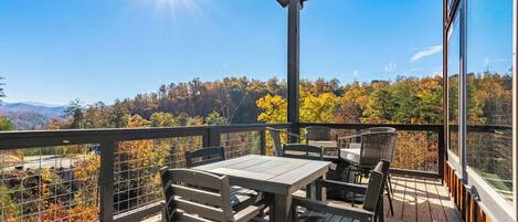 A wooden deck with a table and chairs, overlooking a forested area with autumn foliage.