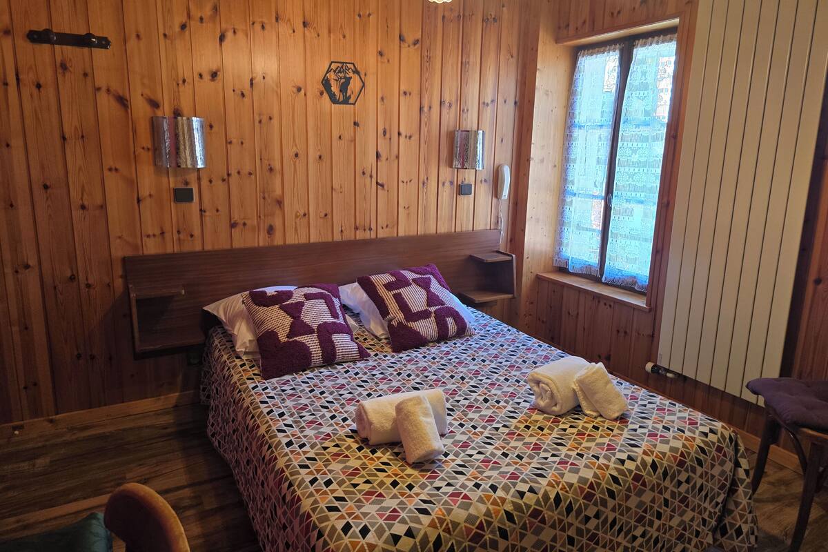 Quarto com painéis de madeira, uma cama, uma janela e um aplique de parede.