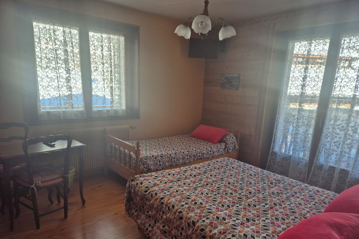 Quarto com duas camas, uma mesa de madeira e uma cadeira.