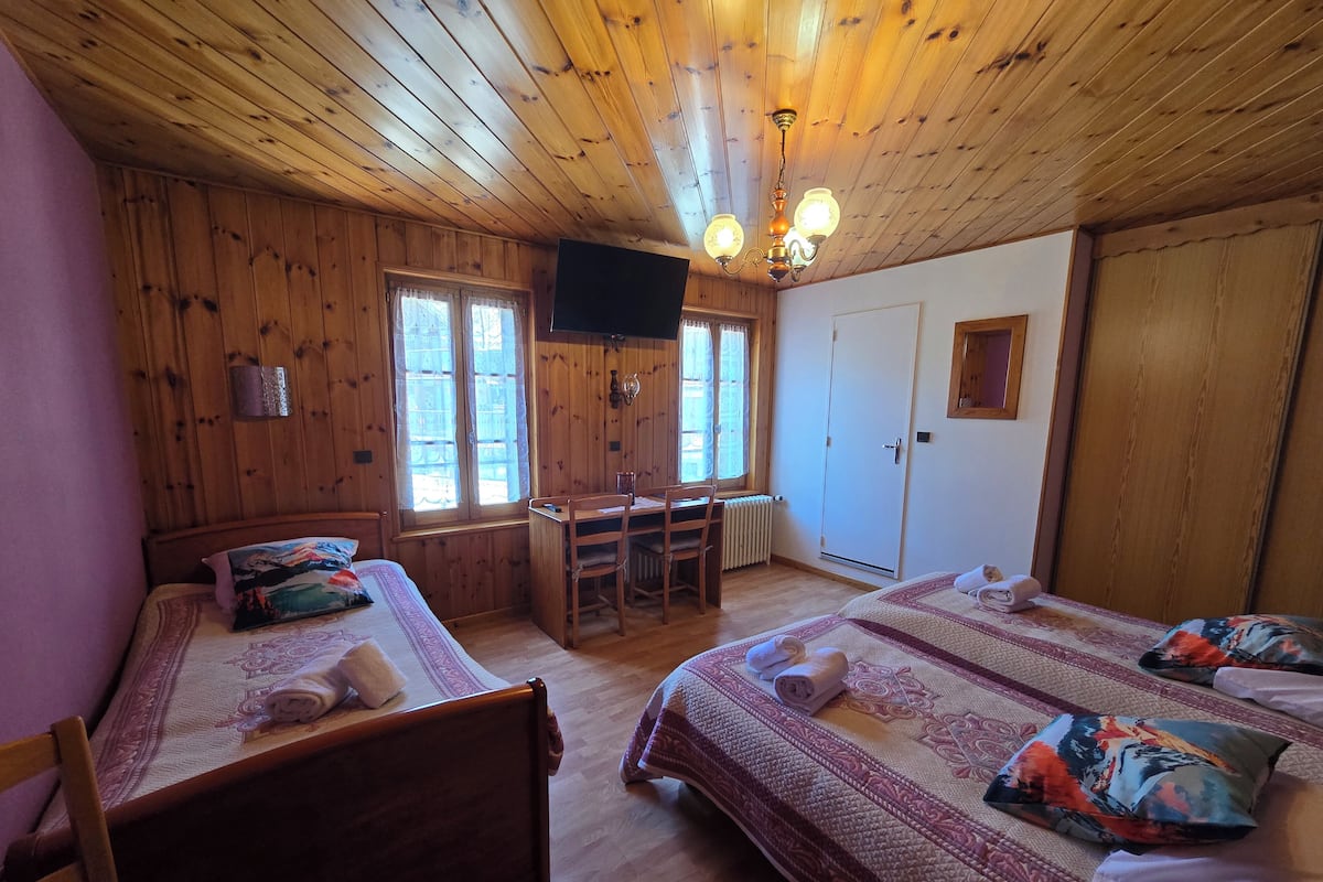 Quarto com painéis de madeira, duas camas, uma escrivaninha e uma televisão.