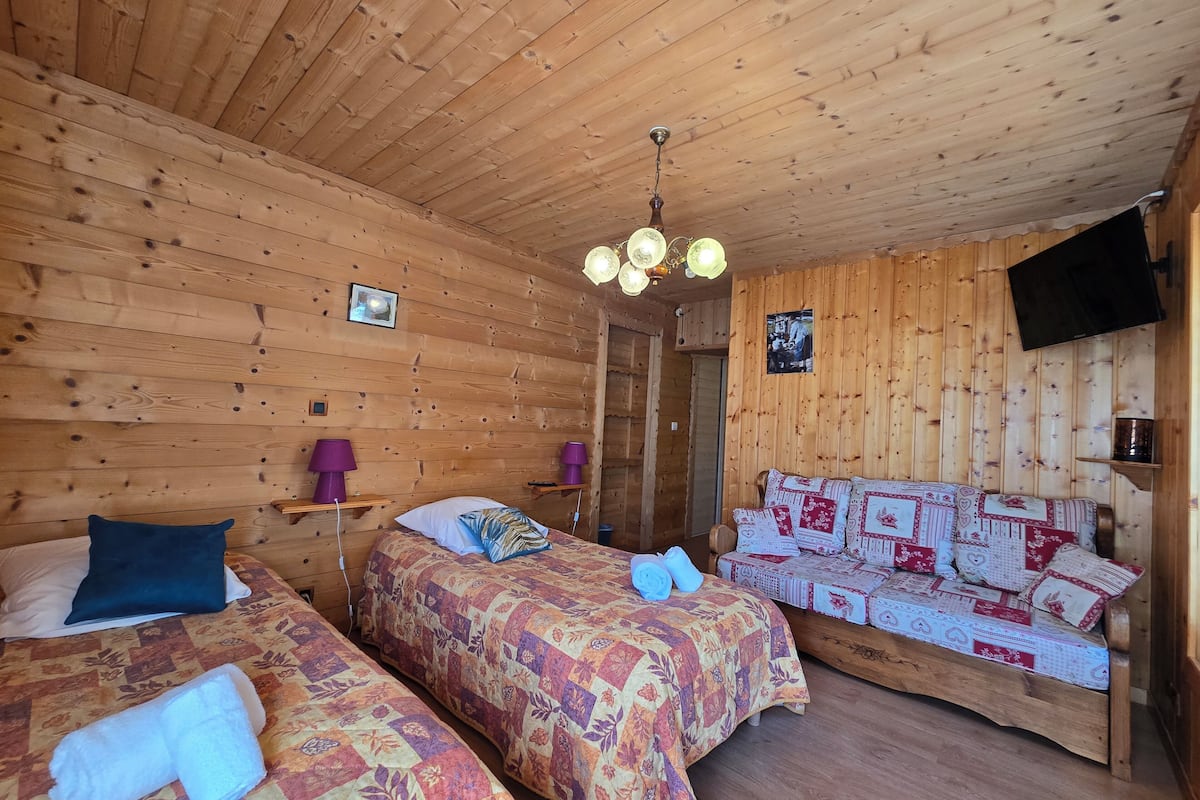 Quarto de cabana de madeira com duas camas, uma luminária no teto, televisão e parede de madeira.