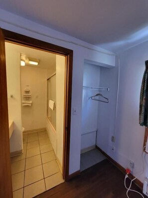 A room with a wooden floor, a white door leading to a bathroom, and a white wall with a towel rack. - Daniel's Motel (La Salle)