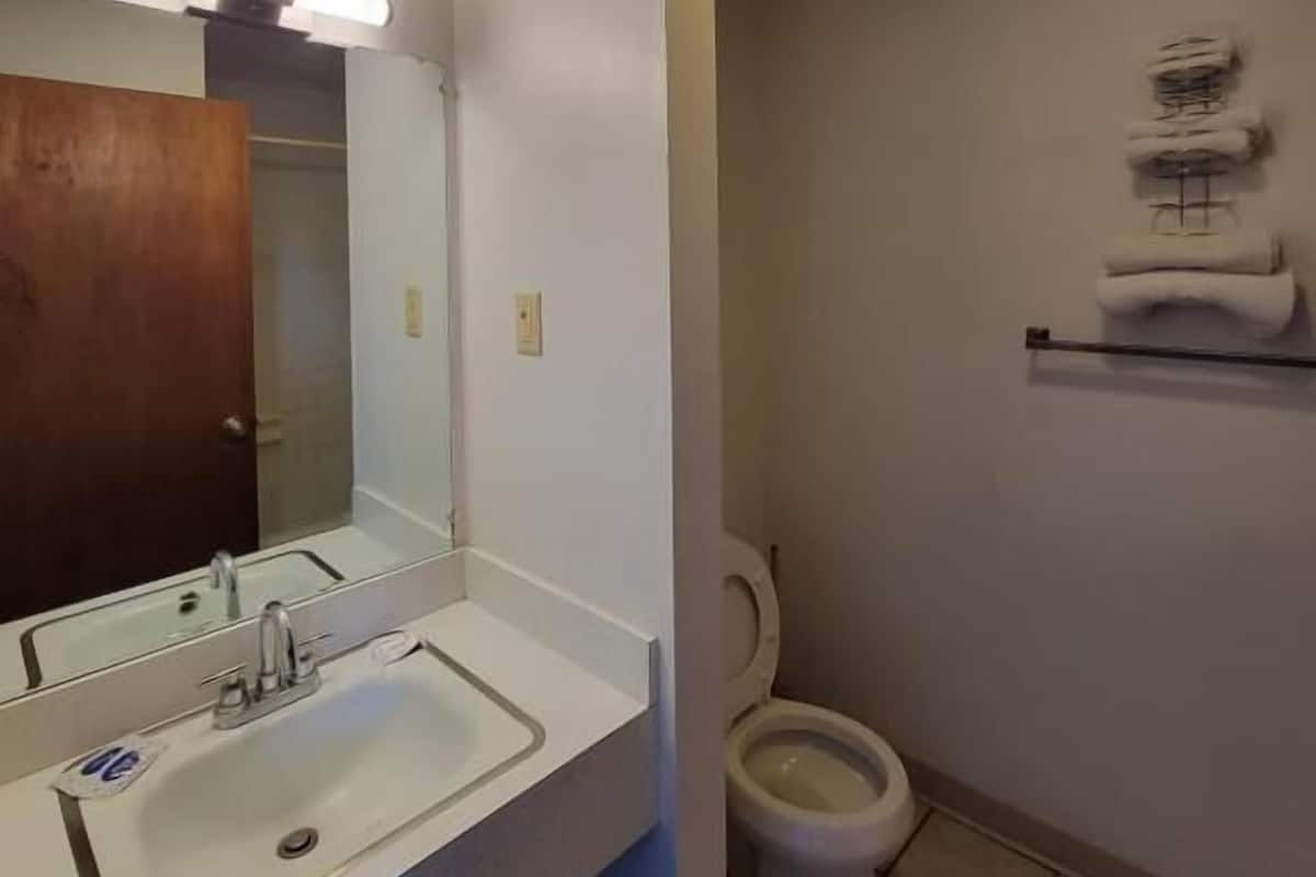 A bathroom with a white sink, mirror, and toilet. There is a towel rack above the toilet and a light fixture on the ceiling.
