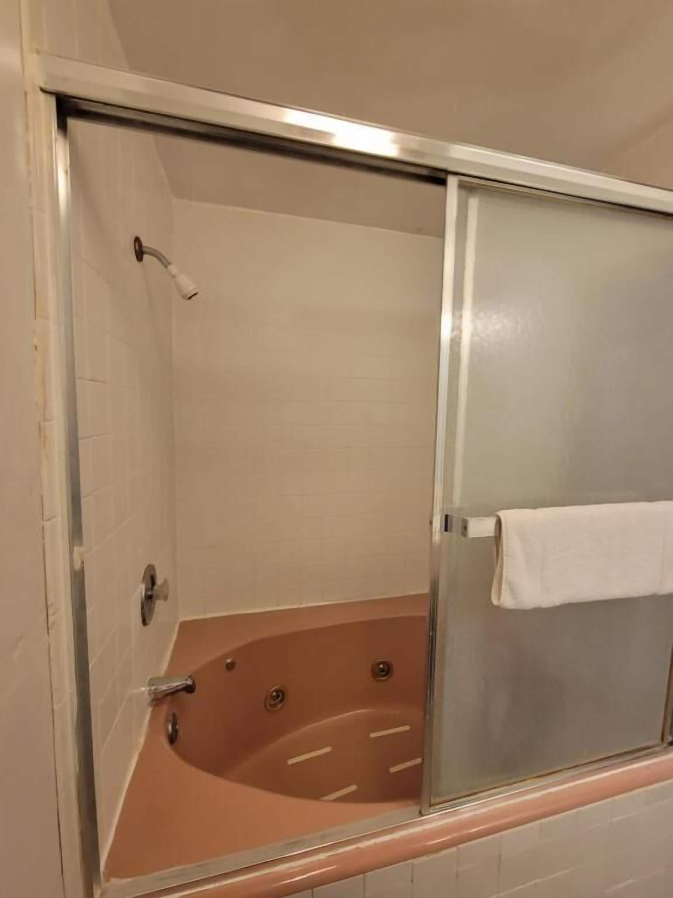 A glass-enclosed jacuzzi with a white towel hanging on the door, beige tiled walls, and a chrome faucet.
