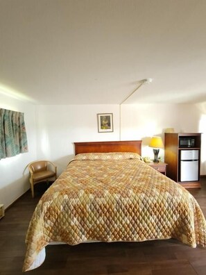 A hotel room with a bed, a chair, a nightstand, a lamp, a refrigerator, and a picture on the wall. - Daniel's Motel (La Salle)