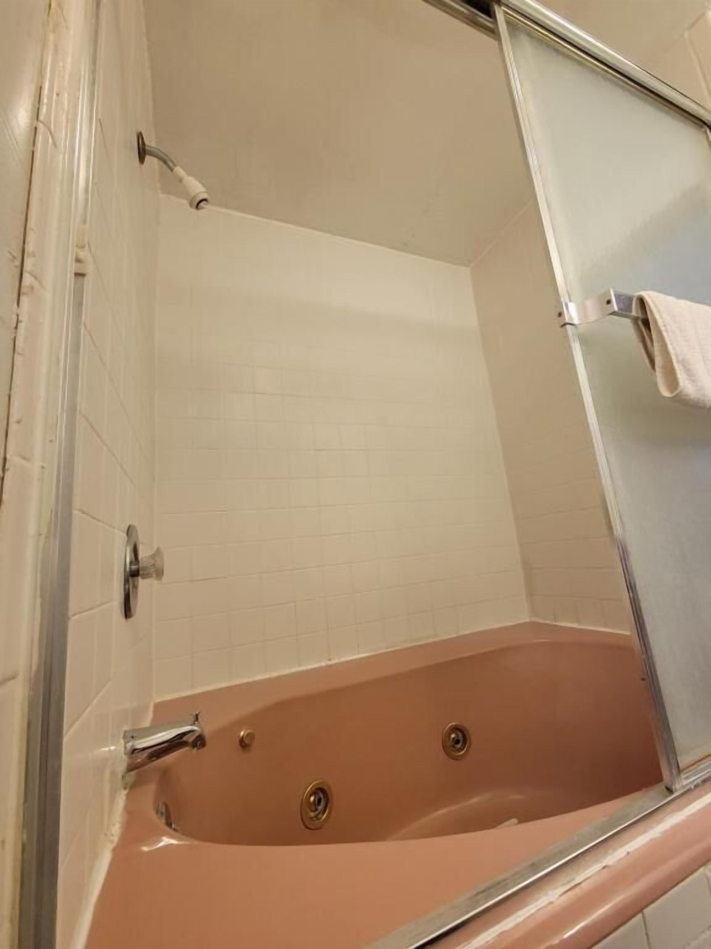 Une salle de bain avec une baignoire entourée de parois en verre, des murs recouverts de carreaux blancs et un porte-serviettes apparent.