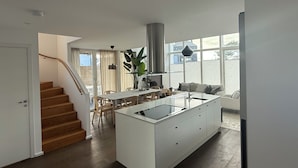 Een moderne keuken met een centraal eiland, een eethoek met stoelen, een trap en een groot raam met uitzicht.